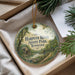 A round ornament with a scenic illustration of Harpeth River State Park in Tennessee, featuring a mill and a bridge, is displayed in a box with pine branches.
