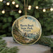 A round ornament with a painting of a coastal landscape, featuring a beach, mountains, and a body of water, hanging from a string.