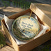 A round ornament in a box, featuring a scenic landscape of Harris Beach State Park, Oregon.
