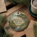A decorative ornament featuring a scenic image of Hartman Creek State Park in Wisconsin, with a deer and a canoe in the foreground. The ornament is hanging on a wooden surface, surrounded by pine branches and a cup of coffee.