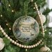 A round ornament hanging on a Christmas tree, featuring a scenic image of a lake and surrounding landscape.
