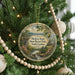 A round ornament hanging on a Christmas tree, featuring a scenic landscape with a river, mountains, and trees.
