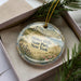 A decorative ornament in a box, featuring a scenic landscape with a lighthouse and a beach, with the text "Hither Hills State Park, New York" printed on it.