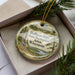 A round ornament with a scenic landscape of Hoffman Hills State Recreation Area, Wisconsin, displayed in a box with pine branches.