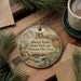A round ornament with a bird and desert landscape design, hanging on a wooden surface.