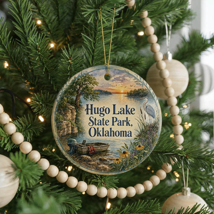 A round ornament hanging on a Christmas tree, featuring a scenic landscape with a lake, trees, and a boat.
