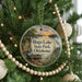 A round ornament hanging on a Christmas tree, featuring a scenic landscape with a lake, trees, and a boat.
