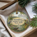 A decorative ornament with a nature-themed design, featuring a bird, flowers, and a pond, is displayed in a box with pine branches.