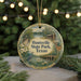 A round ornament with a painting of a park scene, featuring a deer, a bird, and a bridge, hanging from a string.