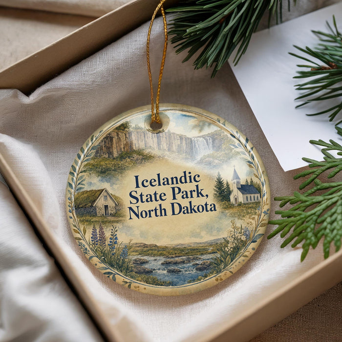 A decorative ornament with a scenic landscape of Iceland, featuring a castle, a river, and mountains, is displayed in a box with pine branches.