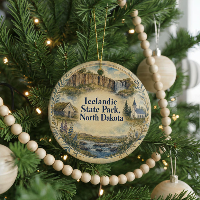 A round ornament on a Christmas tree, featuring a scenic landscape of Iceland, including a waterfall and a church, with the text "Icelandic State Park, North Dakota" displayed prominently.