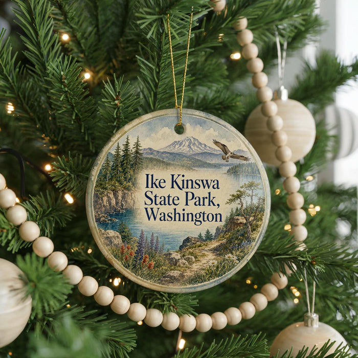 A round ornament hanging on a Christmas tree, featuring a scenic landscape with mountains, trees, and a lake.