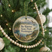 A round ornament hanging on a Christmas tree, featuring a scenic landscape with mountains, trees, and a lake.