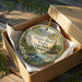 A decorative ornament in a box, featuring a scenic image of the Illinois River, Folsks State Park, and Oregon.