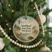 A round ornament hanging on a Christmas tree, featuring a lighthouse and a deer in a grassy field.