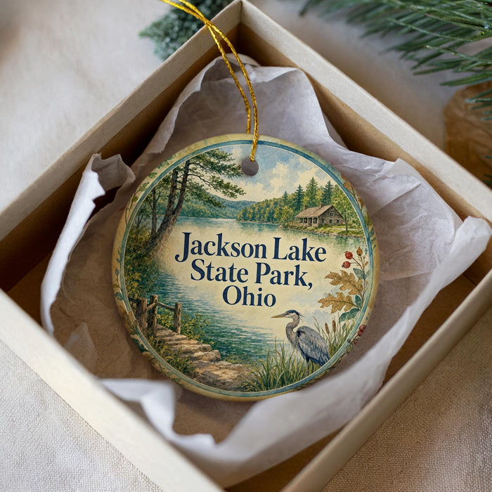 A round ornament with a scenic lake and forest landscape, featuring a bird in the foreground, is displayed in a box.