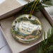 A decorative ornament in a box, featuring a scenic landscape with a waterfall and a building, with the text "James Baird State Park, New York" prominently displayed.