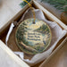 A round ornament with a scenic landscape of trees, a lake, and a bird is displayed in a box.