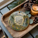 A wooden tray with a decorative ornament featuring a scenic landscape, including a waterfall and pine trees, along with pine cones and a lit candle.