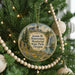 A round ornament hanging on a Christmas tree, featuring a scenic landscape with mountains, a waterfall, and a meadow.