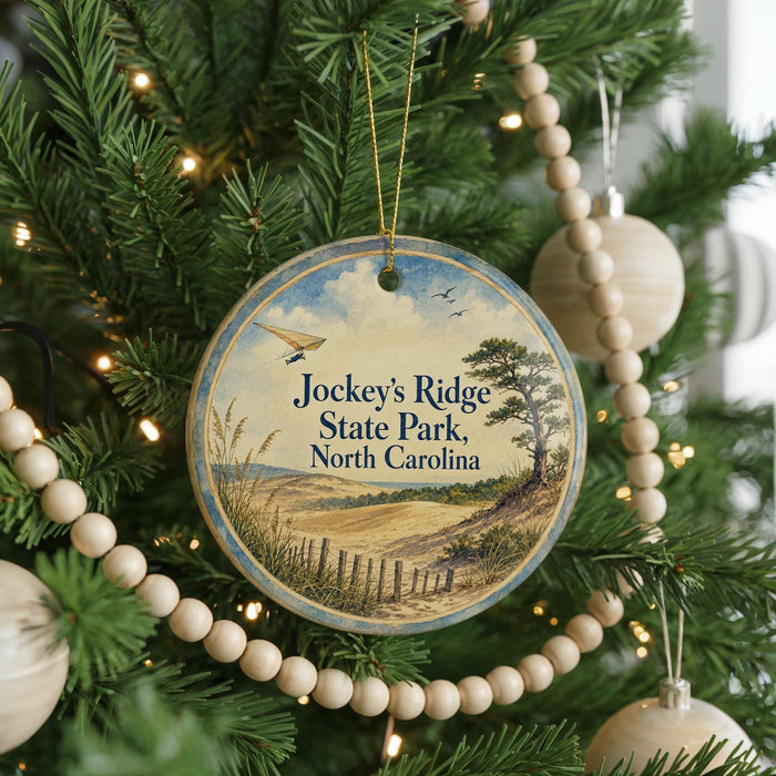 A round ornament hanging on a Christmas tree, featuring a scenic landscape with a tree, field, and birds in the sky.