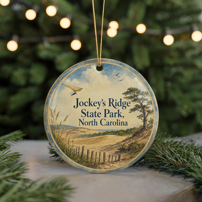 A round ornament with a scenic landscape of Jockey's Ridge State Park, North Carolina, featuring a beach, mountains, and a bird in flight.