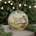 A round ornament with a scenic landscape of Jockey's Ridge State Park, North Carolina, featuring a beach, mountains, and a bird in flight.