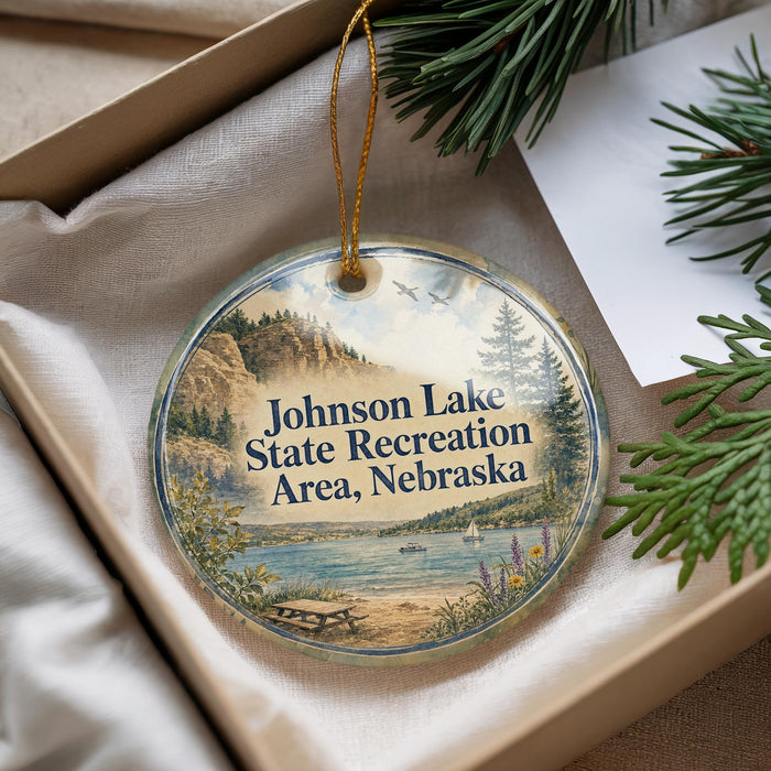 A round ornament with a scenic landscape of Johnson Lake State Recreation Area, Nebraska, featuring a lake, mountains, pine trees, and a boat on the water.