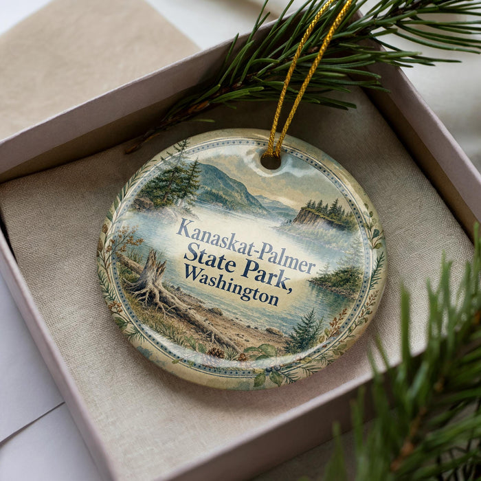 A decorative ornament in a box, featuring a scenic landscape with mountains, pine trees, and a body of water.