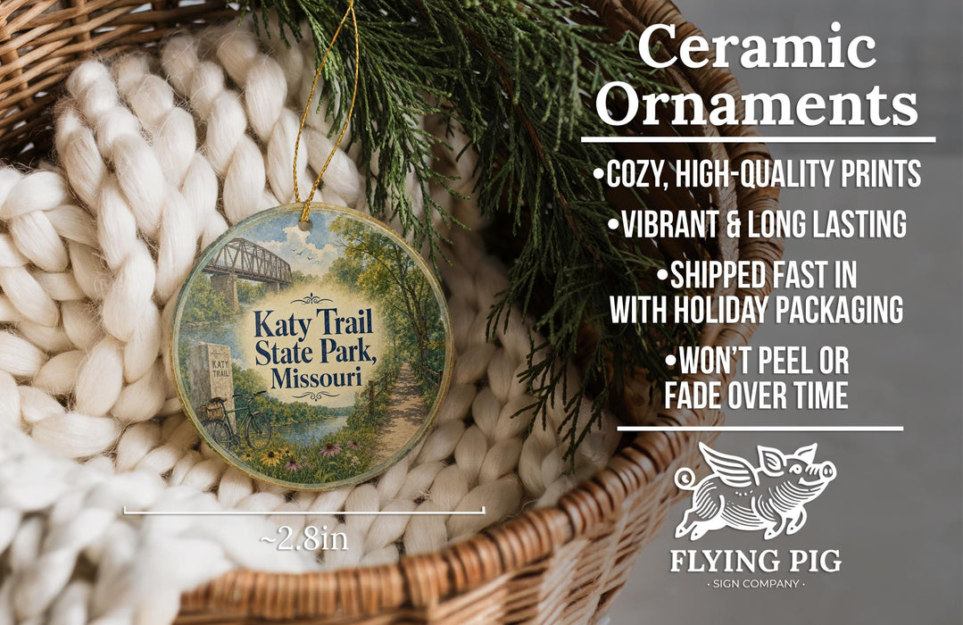 Ceramic ornaments, featuring a detailed image of a scenic trail at Katy Trail State Park, Missouri. The ornaments are described as cozy, high-quality prints, vibrant, and long-lasting, and are shipped fast in holiday packaging. They are not to be peeled or faded over time. The image is a close-up of the ornaments, with a wicker basket and greenery in the background.