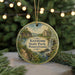 A round ornament with a scenic image of Keystone State Park, Pennsylvania, featuring a waterfall and a house, is displayed on a table with pine branches in the background.
