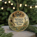 A round ornament with a picture of a cave and a windmill, surrounded by greenery, hangs in front of a blurred background with twinkling lights.