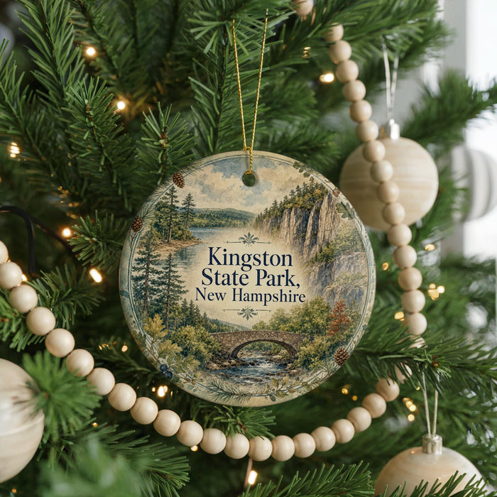 A round ornament hanging on a Christmas tree, featuring a scenic landscape with a bridge and pine trees.