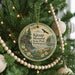 A round ornament hanging on a Christmas tree, featuring a scenic landscape with a lake, mountains, and a cabin.
