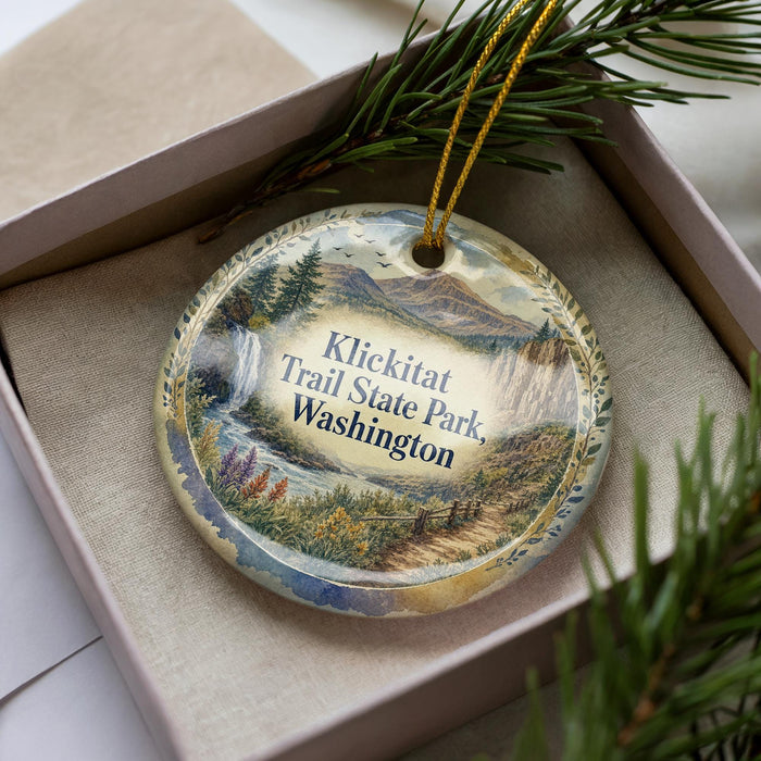 A decorative ornament in a box, featuring a scenic landscape with mountains, waterfalls, and pine trees.