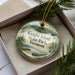 A decorative ornament in a box, featuring a scenic landscape with a lake, mountains, and pine trees.