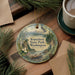 A decorative ornament featuring a scenic landscape of Kopachuck State Park in Washington, surrounded by pine branches and a cup of coffee on a wooden surface.