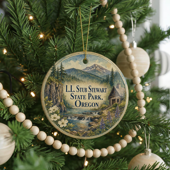 A round ornament hanging on a Christmas tree, featuring a scenic landscape with mountains, a river, and a cabin.
