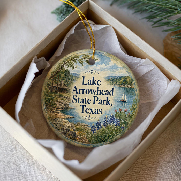 A decorative ornament in a box, featuring a scenic landscape with a lake, trees, and a sailboat.