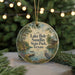 A round ornament with a painting of Lake Bob Sandlin State Park in Texas, featuring a bird and a dock, is displayed on a table with pine branches in the background.