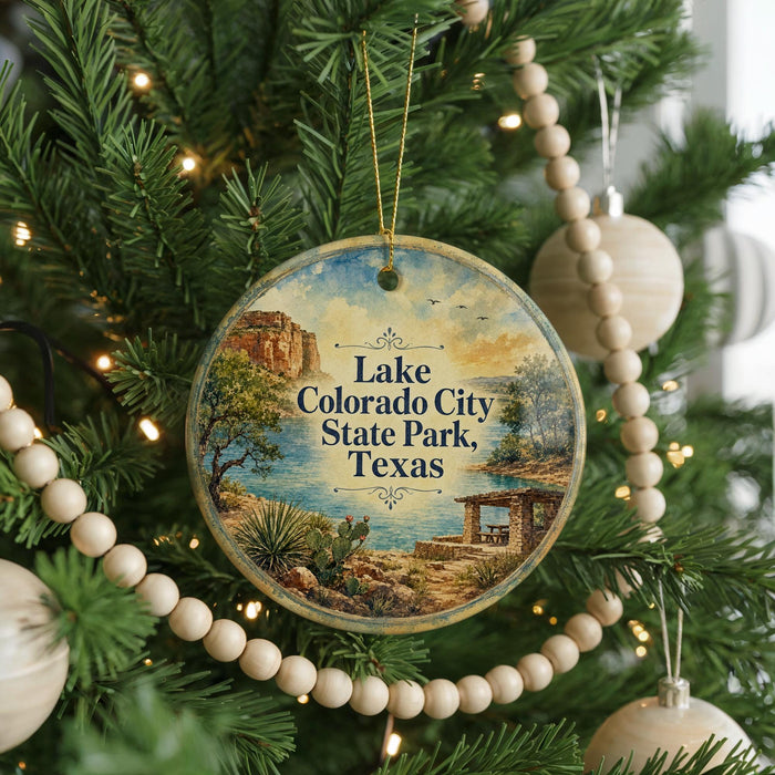 A round ornament hanging on a Christmas tree, featuring a scenic landscape with a lake, mountains, and a desert.
