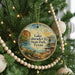 A round ornament hanging on a Christmas tree, featuring a scenic landscape with a lake, mountains, and a desert.