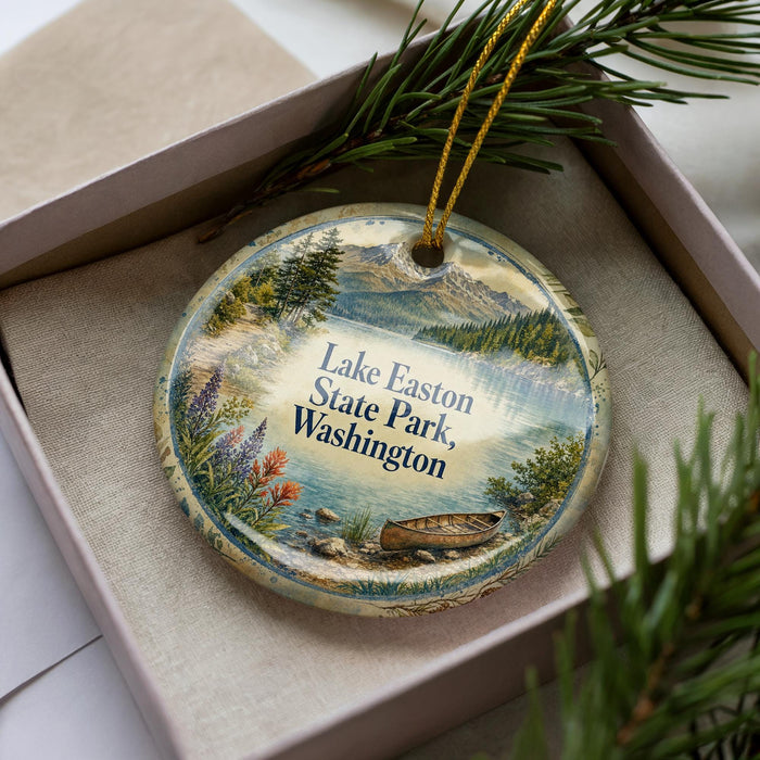 A decorative ornament in a box, featuring a scenic landscape with a lake, mountains, and pine trees.