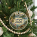 A round ornament hanging on a Christmas tree, featuring a scenic landscape with a lake, mountains, and a boat.