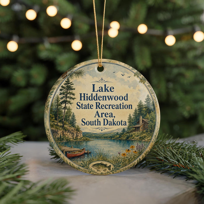 A round ornament with a scenic image of Lake Hiddenwood State Recreation Area in South Dakota, featuring a lake, pine trees, and a cabin.