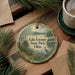 A decorative ornament featuring a scenic lake landscape with a bird, surrounded by pine branches and a cup of coffee on a wooden surface.