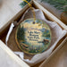 A decorative ornament in a box, featuring a scenic landscape with mountains, a lake, and a cabin.