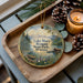 A wooden tray with a decorative ornament featuring a scenic landscape of Lake Mary Ronan State Park, Montana, and pine cones.