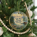 A round ornament hanging on a Christmas tree, featuring a scenic landscape with mountains, a lake, and a wooden dock.