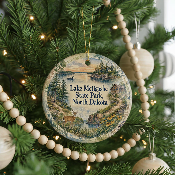 A round ornament hanging on a Christmas tree, featuring a scenic landscape with a lake, trees, and a house.